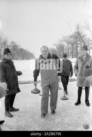 Dan Blocker, who plays the role of Hoss Cartwright in the television series Bonanzna, here in the center, with an ice stock in his hand while curling on the Nymphenburg Canal. Around him are some players. Stock Photo