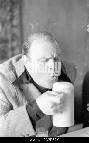 Dan Blocker, who plays the role of Hoss Cartwright in the Bonanza television series, holds a mug of beer and blows away the foam. Stock Photo