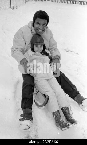 Roberto Blanco plays in the snow with his daughter Mercedes and a sled in 1970. Stock Photo