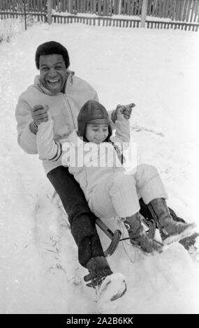 Roberto Blanco plays in the snow with his daughter Mercedes and a sled in 1970. Stock Photo