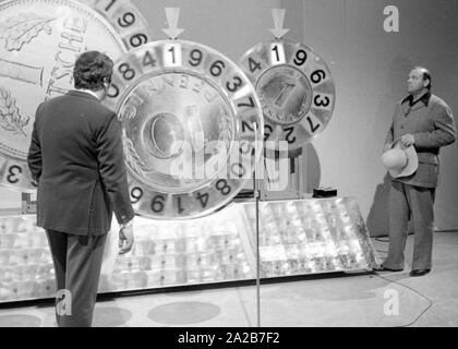 Wim Thoelke and the impersonator of Hoss from the television series Bonanza, Dan Blocker, in the television show 3x9. The lucky wheels in the form of the German Mark and the Pfenning are the symbols of the Aktion Sorgenkind. Stock Photo