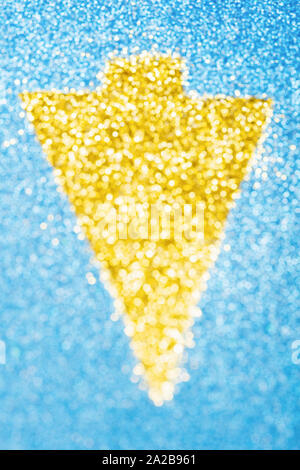 Abstract photo of golden arrow made of glitter on sparkly blue paper, selective focus Stock Photo