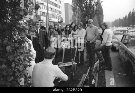 A painter, surrounded by a crowd, makes a painting on the grass verge in the Leopoldstrasse. In the background, the 'Citta 2000' complex, a shopping and entertainment center. Stock Photo