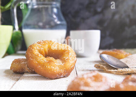 Spanish roscos or donuts at breakfast on a white wooden table next to a cup of coffee and a jar of milk. Black background and empty copy space. Stock Photo