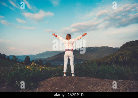 Happy celebrating winning success woman in white clothes standing elated with arms raised up above her head in celebration of having reached mountain Stock Photo