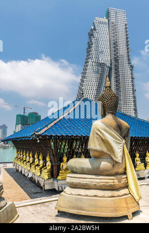 A Buddhist statue at the Seema Malaka Temple on Lake Beira sits against a background of urban development in the Sri Lankan capital of Columbo. Stock Photo