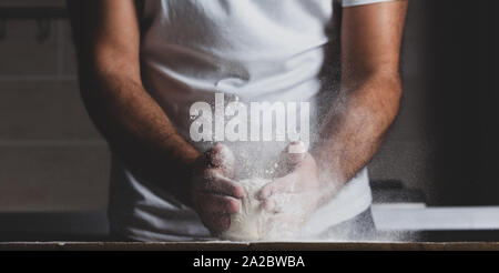 Man kneads raw dough, dust from flour flies in different directions, male hands on a black background Stock Photo