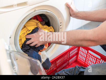 close-up of man loading colored clothes in washing machine Stock Photo