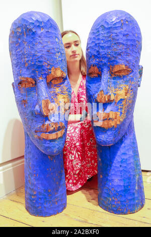 Somerset House, London, UK, 02 Oct 2019. An assistant poses with the wooden sculptures 'Blue Heads' by artist Prince Gyasi, presented by Nil Gallery Paris. Somerset House, in partnership with 1-54, presents the Contemporary African Art Fair, now in its 7th year at Somerset House. The Fair runs from Oct 3-6 and brings together 45 leading galleries with over 140 artists. Credit: Imageplotter/Alamy Live News Stock Photo