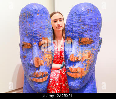 Somerset House, London, UK, 02 Oct 2019. An assistant poses with the wooden sculptures 'Blue Heads' by artist Prince Gyasi, presented by Nil Gallery Paris. Somerset House, in partnership with 1-54, presents the Contemporary African Art Fair, now in its 7th year at Somerset House. The Fair runs from Oct 3-6 and brings together 45 leading galleries with over 140 artists. Credit: Imageplotter/Alamy Live News Stock Photo