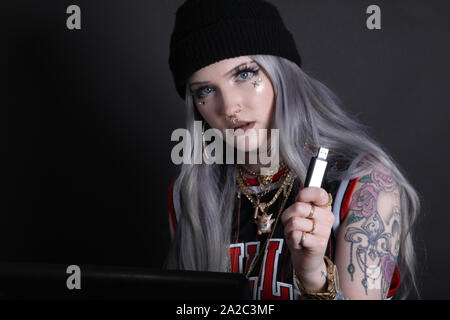 Millennial woman on laptop looking at camera holding a USB key, low key 2019 modern cyber security hacking Stock Photo