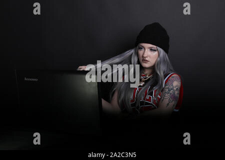 Millennial woman on laptop sitting back looking at screen watching a podcast or live video stream, low key 2019 Stock Photo