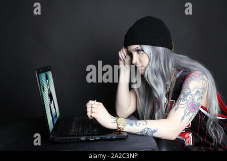 Side view of millennial woman on laptop watching Anonymous hacking group video broadcast on screen, low key 2019 Stock Photo