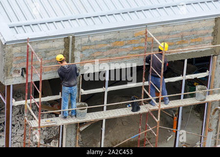 Two construction workers plaster a wall while standing on a scaffold Stock Photo