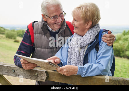 Retired Couple On Walking Holiday Resting On Gate With Map Stock Photo