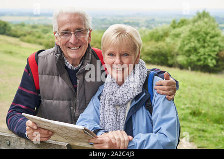 Portrait Of Retired Couple On Walking Holiday Resting On Gate With Map Stock Photo