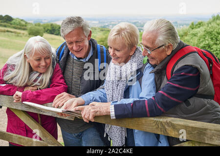 Group Of Senior Friends Hiking In Countryside Standing By Gate  Looking At Map Stock Photo