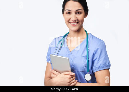 Studio Portrait Shot Of Female Nurse Wearing Scrubs Using Digital Tablet Stock Photo