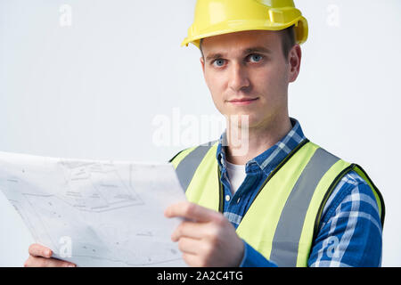 Studio Portrait Of Builder Architect Looking At Plans Against White Background Stock Photo