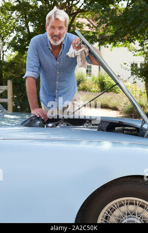 Portrait Of Mature Man Working On Engine Under Hood Of  Restored Classic Sports Car Outdoors Stock Photo