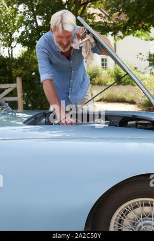 Mature Man Working On Engine Under Hood Of  Restored Classic Sports Car Outdoors At Home Stock Photo