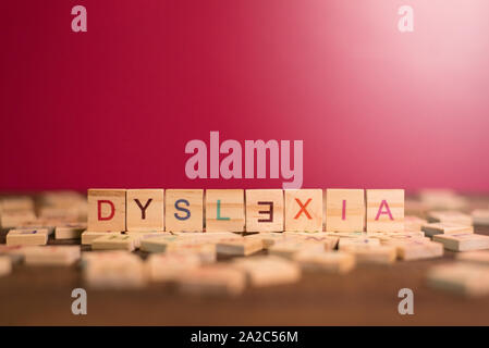 wooden alphabet blocks with DYSLEXIA word in the center on wooden table against pink background. Concept of Dyslexia awareness and human brain develop Stock Photo