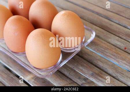 close up Six brown eggs in plastic box on bamboo table with one broken boiled egg, top view. Stock Photo