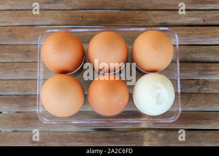 close up Six brown eggs in plastic box on bamboo table with one broken boiled egg, top view. Stock Photo