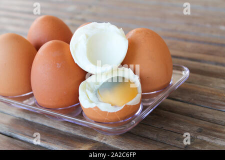 close up Six brown eggs in plastic box on bamboo table with one broken boiled egg, top view. Stock Photo