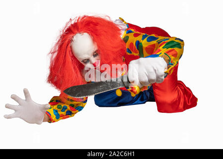 bad clown lies on the ground and holds a knife in the camera Stock Photo