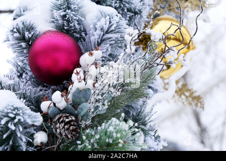 Golden and red Christmas balls with cones on fir branches on winter street. New Year decorations covered with snow, festive ornaments in city Stock Photo