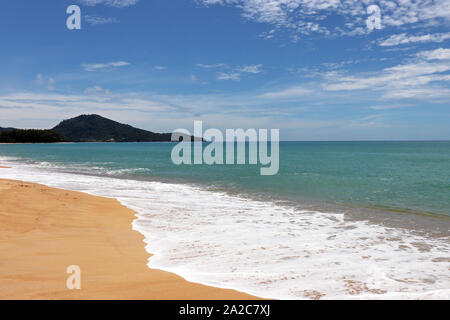 Tropical sandy beach, scenic view to empty sea coast with yellow sand, green forest and mountains. Picturesque seascape with blue sky and white clouds Stock Photo