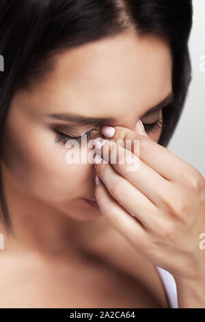 Nose pain. Young woman caught cold. Holds his hand on his nose. Cold. Painful condition. The concept of health. On a gray background.