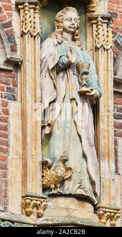 Faded painted statue of St John the evangelist (gospel writer) on the wall above the entrance of St John’s college, university of Cambridge, England. Stock Photo