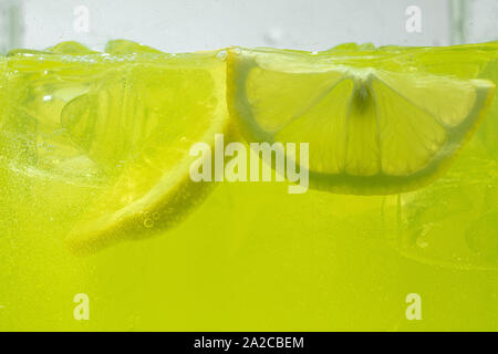 Close up view of the lemon slices in lemonade background. Texture of cooling sweet summer's drink with macro bubbles on the glass wall. Fizzing or floating up to top of surface. Stock Photo