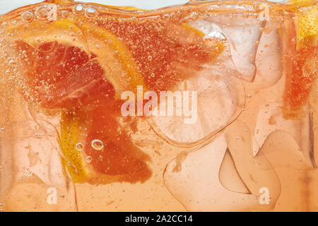 Close up view of the lemon and grapefruit slices in lemonade background. Texture of cooling sweet summer's drink with macro bubbles on the glass wall. Fizzing or floating up to top of surface. Stock Photo
