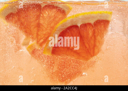 Close up view of the lemon and grapefruit slices in lemonade background. Texture of cooling sweet summer's drink with macro bubbles on the glass wall. Fizzing or floating up to top of surface. Stock Photo