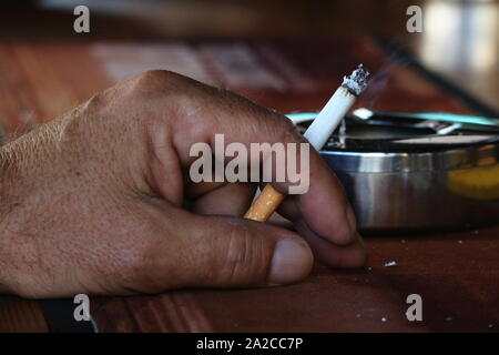 Close up of man's hand holding lit cigarette on a wood bar Stock Photo