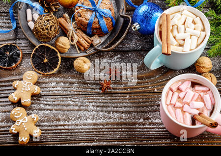 Flat lay Christmas background of two mugs of hot chocolate with marshmallows, spruce branch and tray with gingerbread man cookies on wooden table Stock Photo