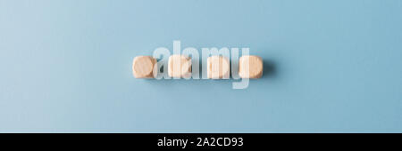 Wide view image of four blank wooden dices placed in a row over light blue background. Stock Photo