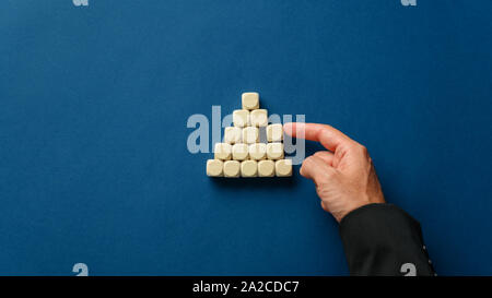 Business executive building a pyramid shape with blank wooden dices over a navy blue background. Stock Photo