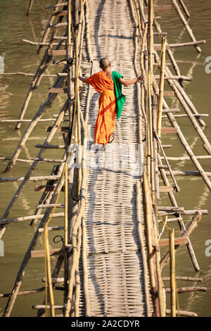 Young Buddhist monk crossing the bamboo footbridge over the Nam Khan River, Luang Prabang, Luang Prabang province, Northern Laos, Laos, Southeast Asia Stock Photo