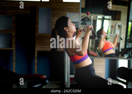 Fit female doing rear lat pull-down under supervision of her