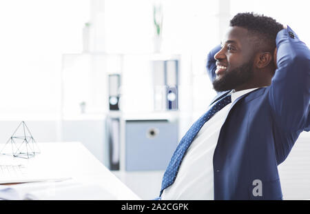 Dreamy african businessman leaning back in modern office Stock Photo