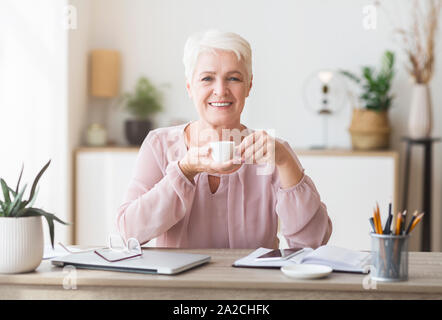 Peaceful aged lady having coffee break while working Stock Photo