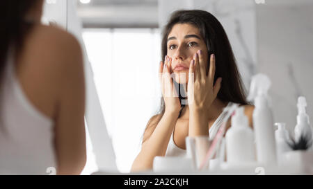 Woman Touching Face Looking At Skin In Mirror At Bathroom Stock Photo