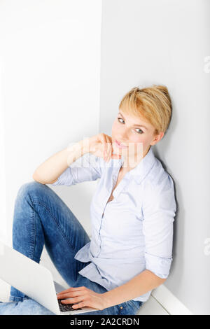 Attractive young woman using her laptop computer sitting on the floor Stock Photo