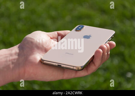 iPhone Xs Max gold smartphone model by Apple Computers close up in male hand on the background of green grass. Italy, Tuscany, Pisa. 26 December 2018 Stock Photo