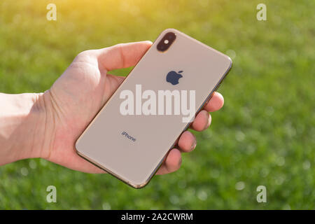 iPhone Xs Max gold smartphone model by Apple Computers close up in male hand on the background of green grass. Italy, Tuscany, Pisa. 26 December 2018 Stock Photo