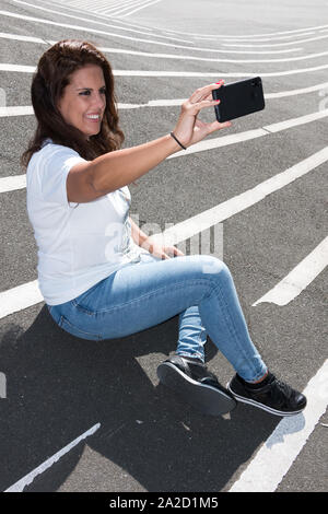 Young woman makes a selfie sitting on the grey floor with white lines. Stock Photo